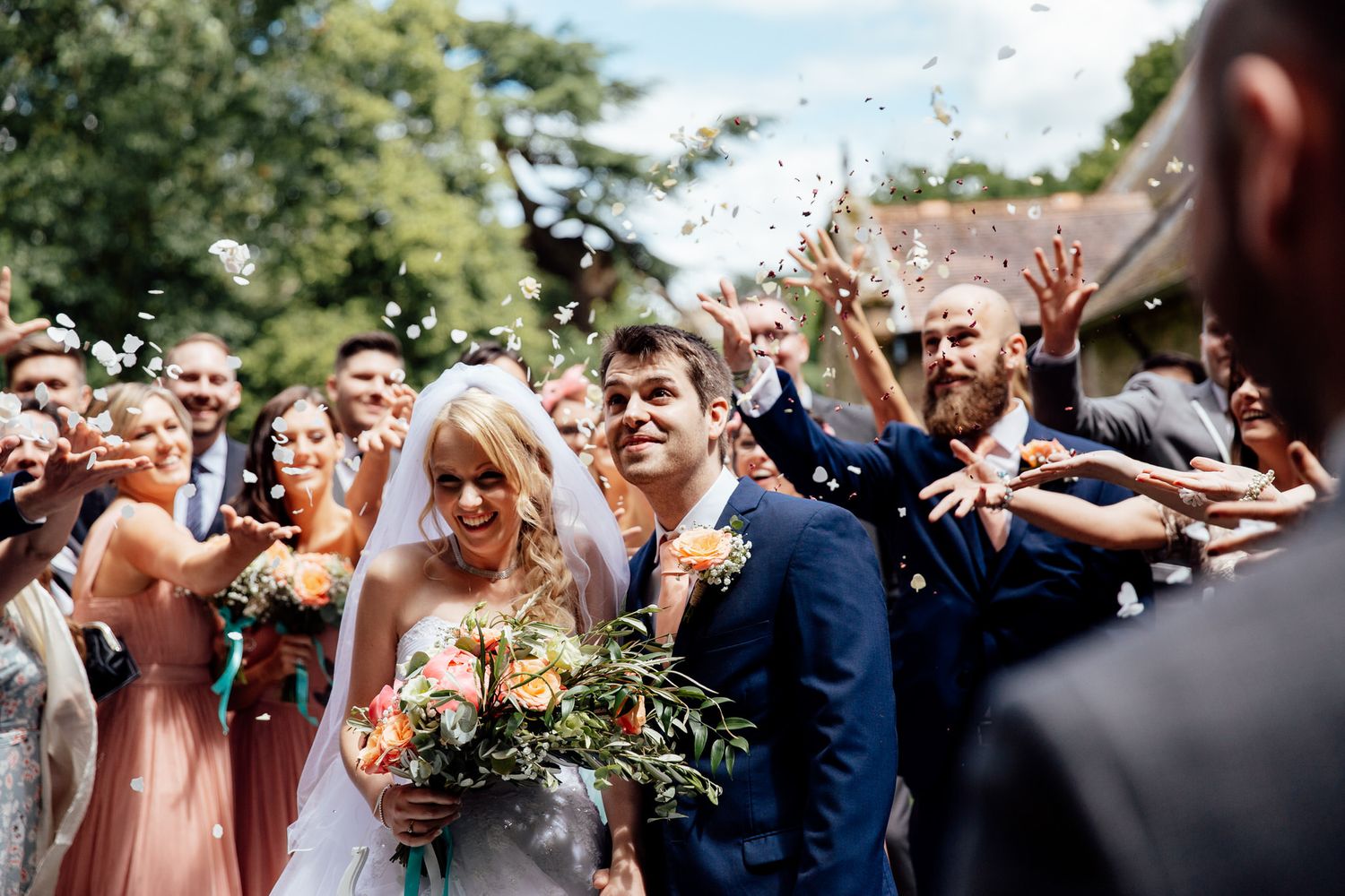 Wedding guests throw confetti during outdoor celebration.