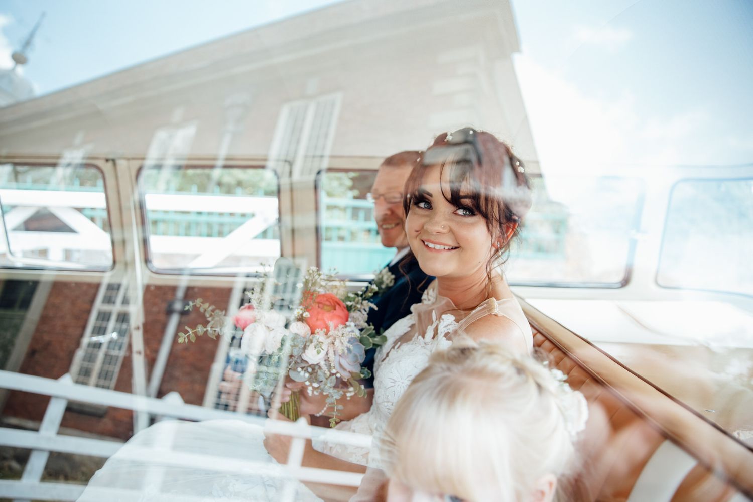 Bride in white dress poses near window in elegant indoor setting with natural lighting.