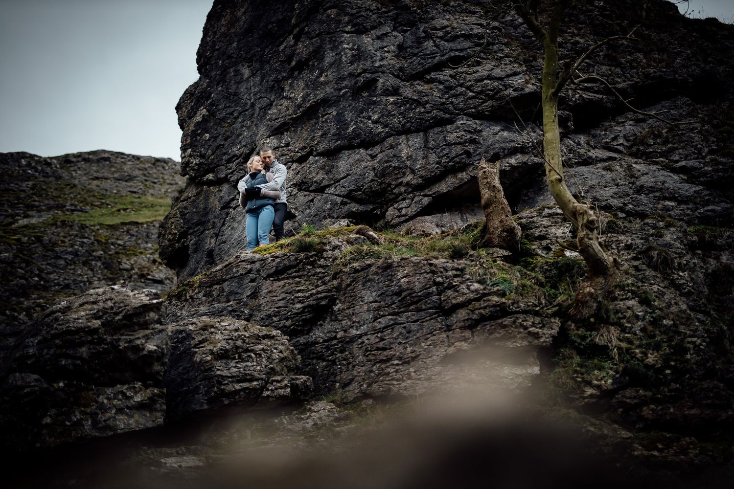 Two people pose among dramatic rock formations in a mountainous landscape.