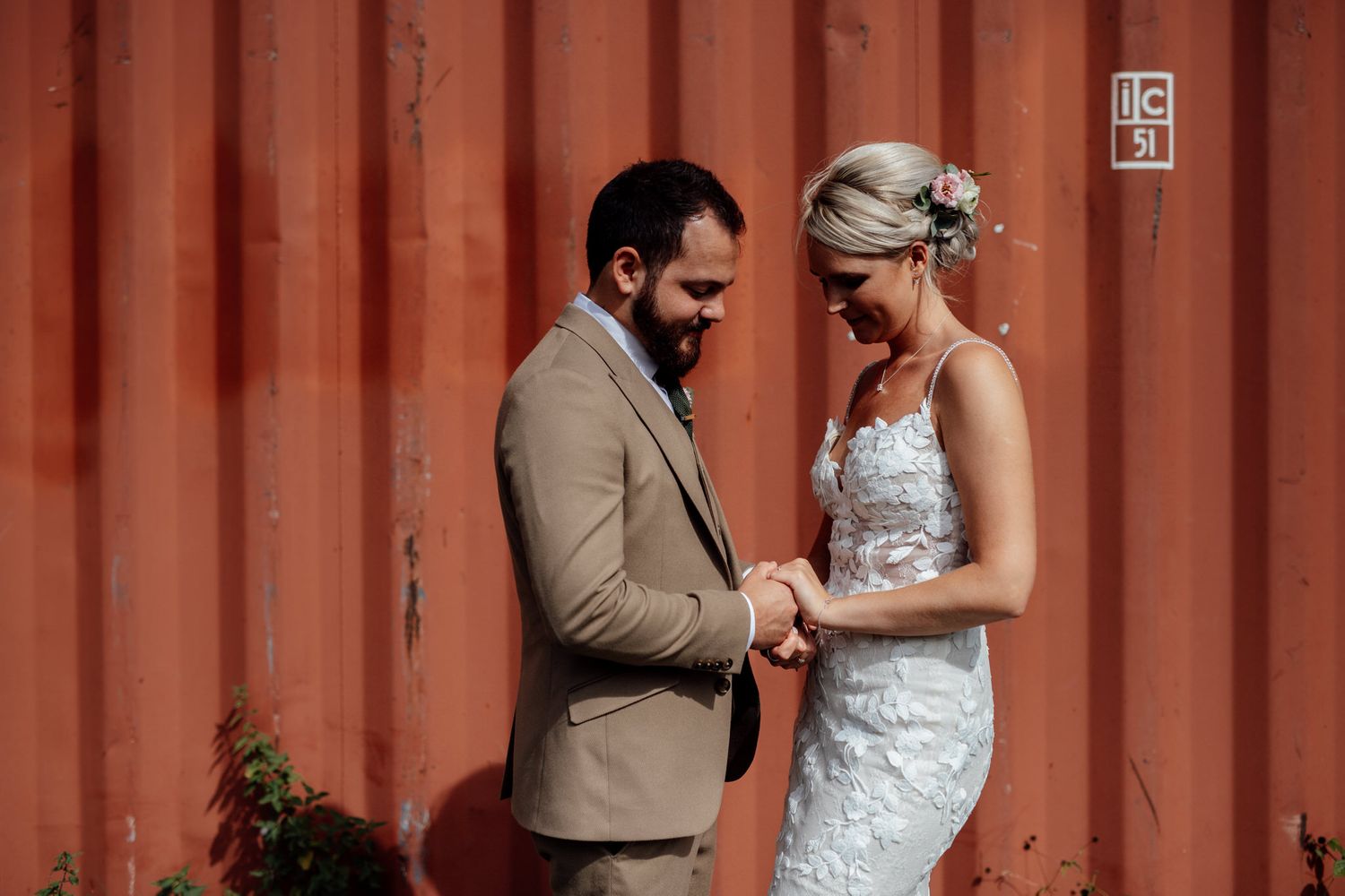 A couple shares an intimate moment against a rustic orange shipping container backdrop.