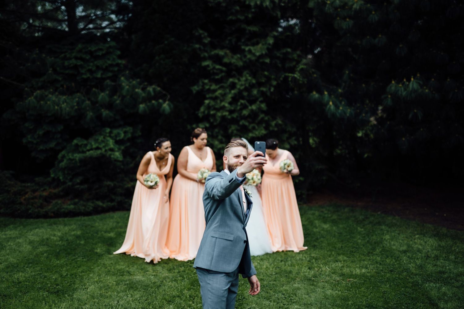 Bridal party in peach dresses walks across green lawn during outdoor photo session.