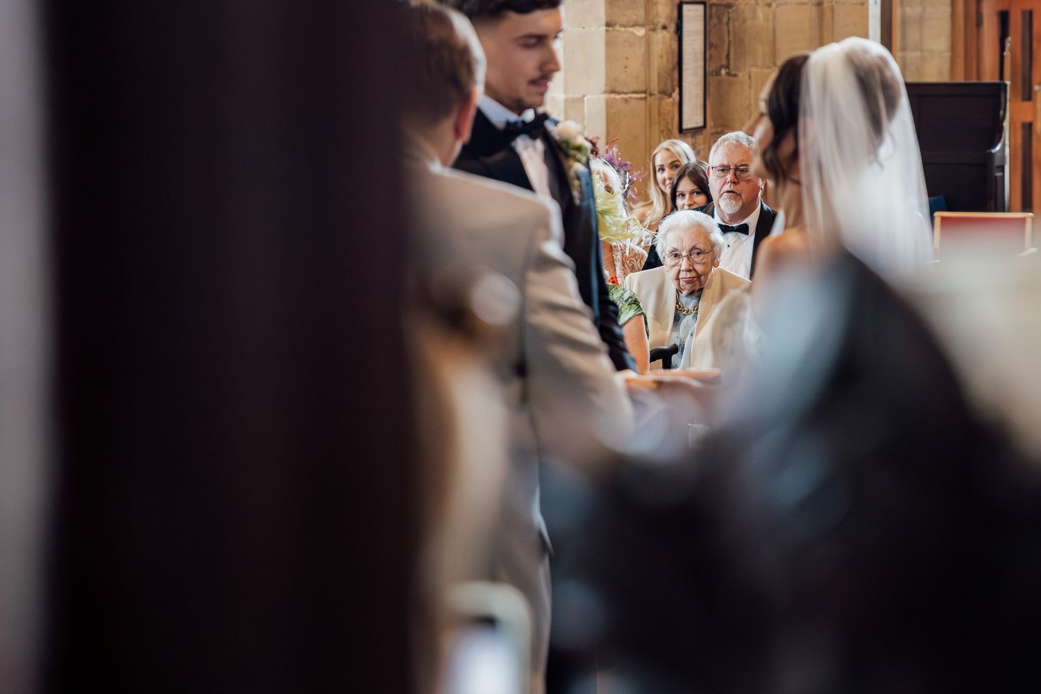 Wedding guests gather in an elegant indoor venue with warm lighting and decorative architectural details.