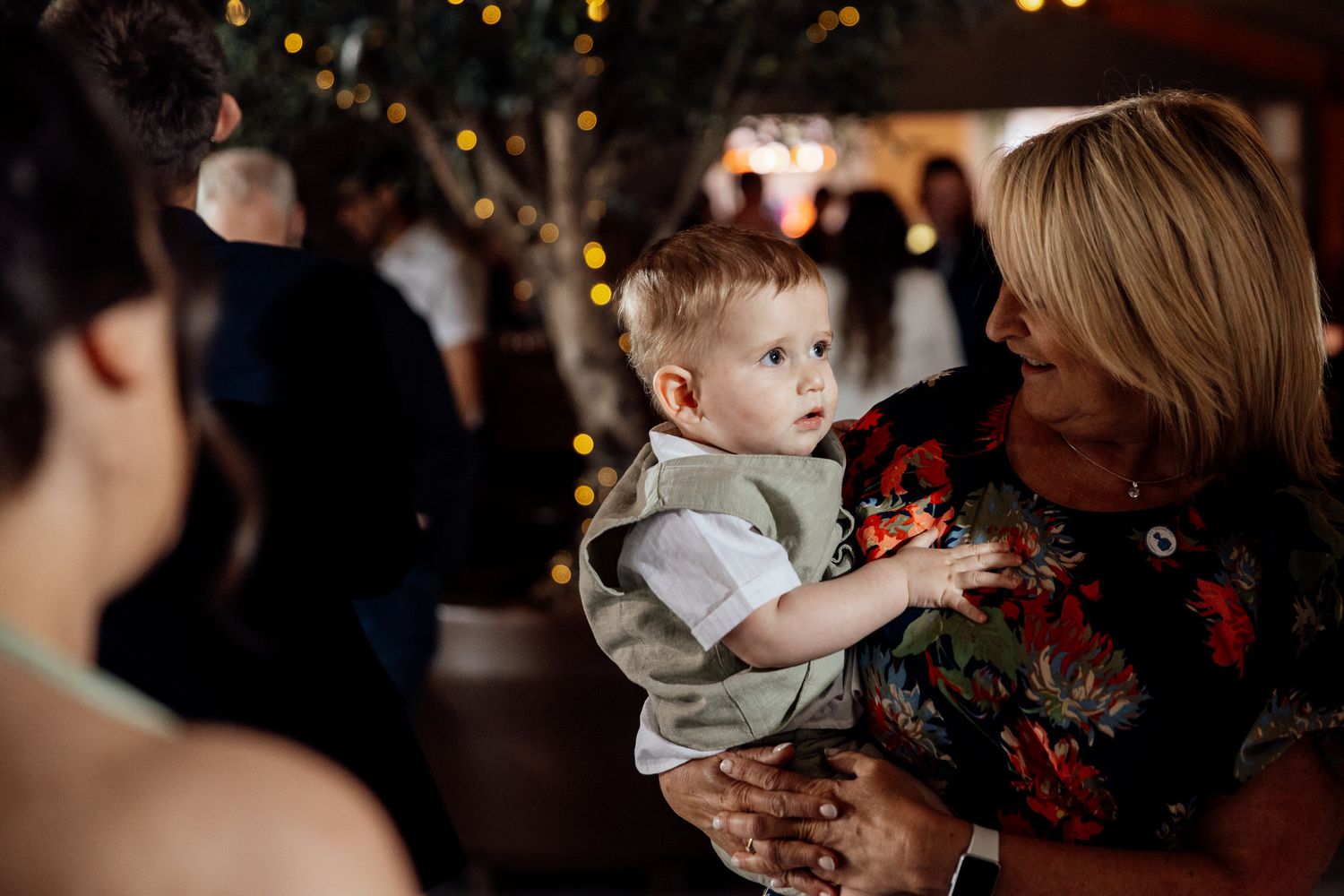 Wedding reception guests dance and celebrate in a dimly lit venue with warm lighting.