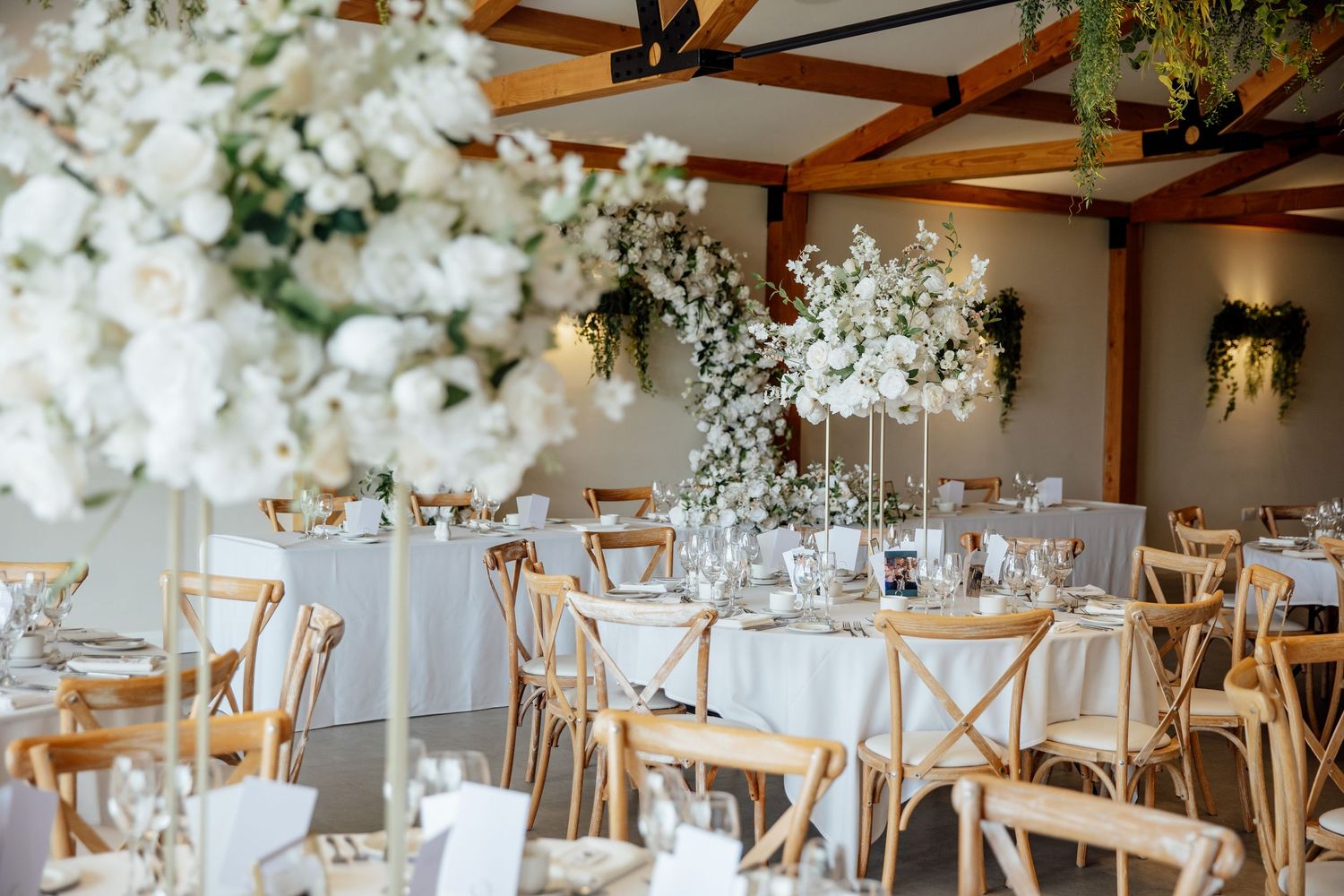 Elegant wedding reception tables decorated with white floral centerpieces and wooden cross-back chairs.