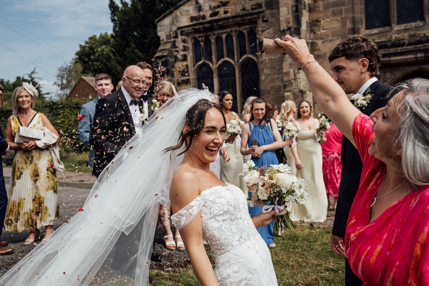 Wedding celebration outside historic church with confetti toss and joyful guests.