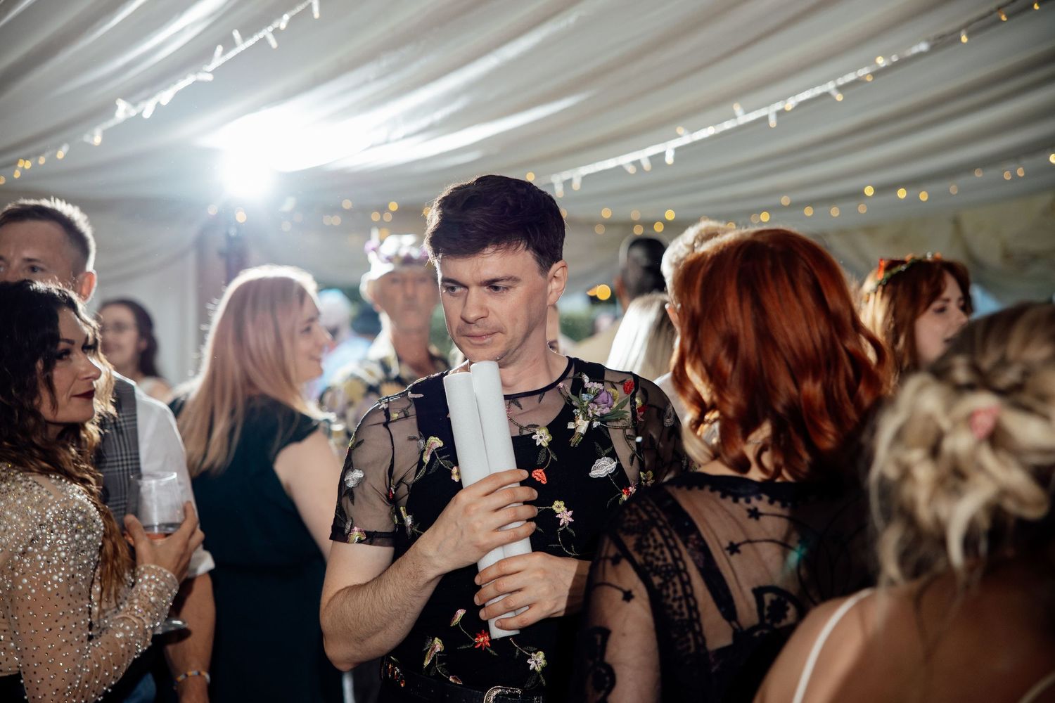 Wedding reception guests dancing and celebrating under white tent lighting.