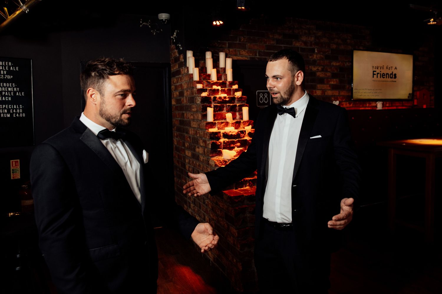 Two people in formal attire having an intimate conversation in a dimly lit venue.