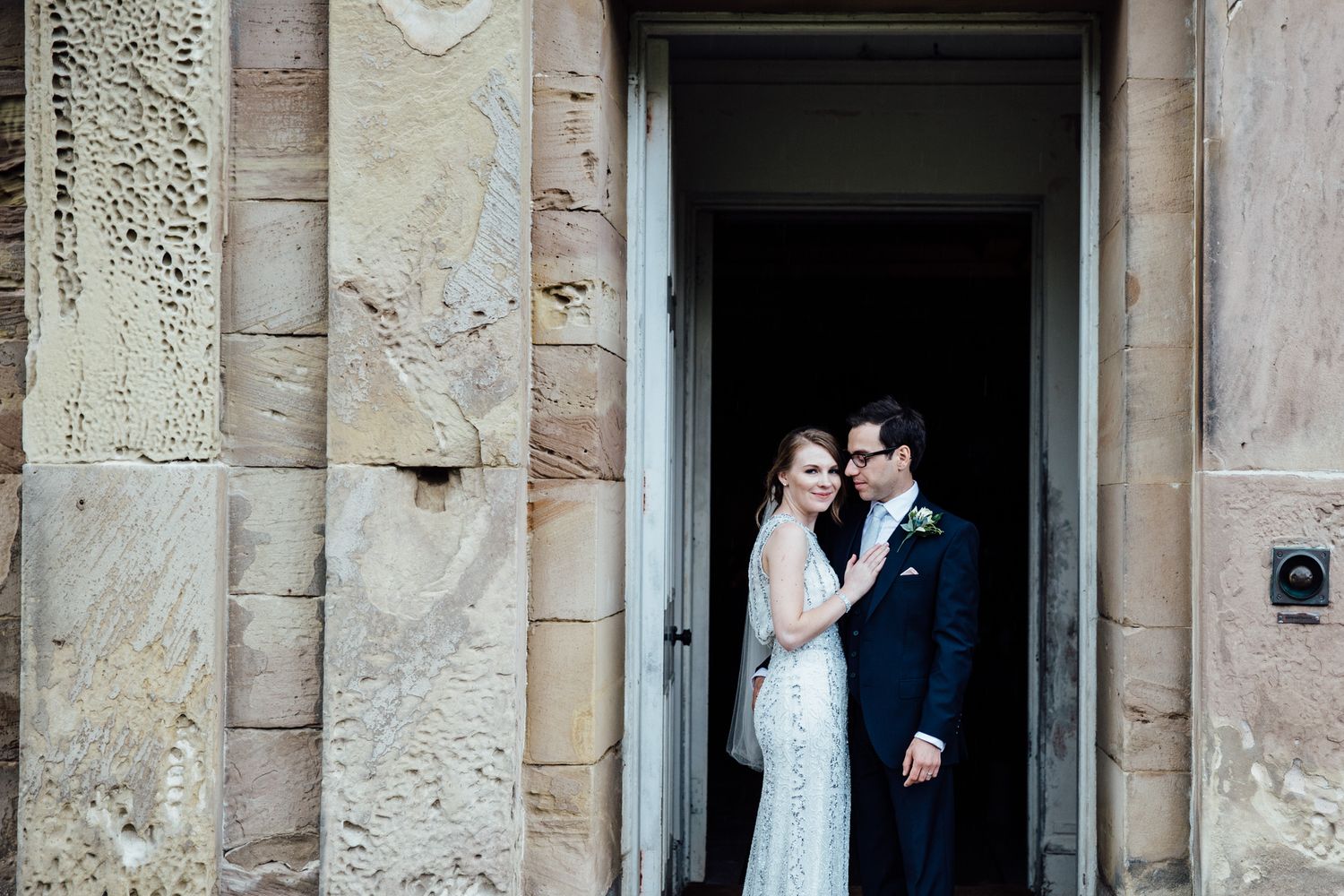 Wedding couple framed by dramatic stone doorways of a historic building.