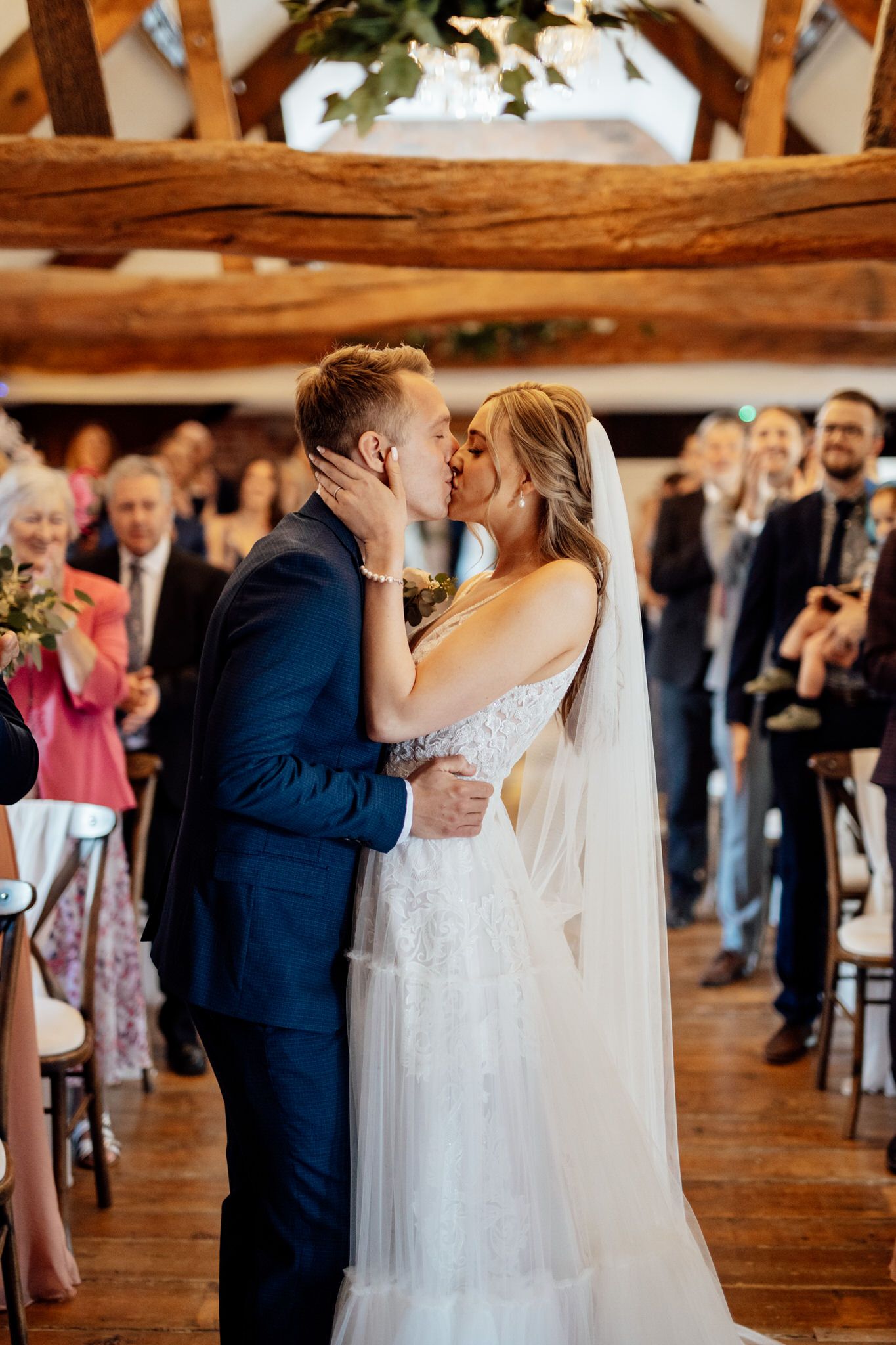 Wedding couple's first dance surrounded by guests in a timber-framed barn venue.