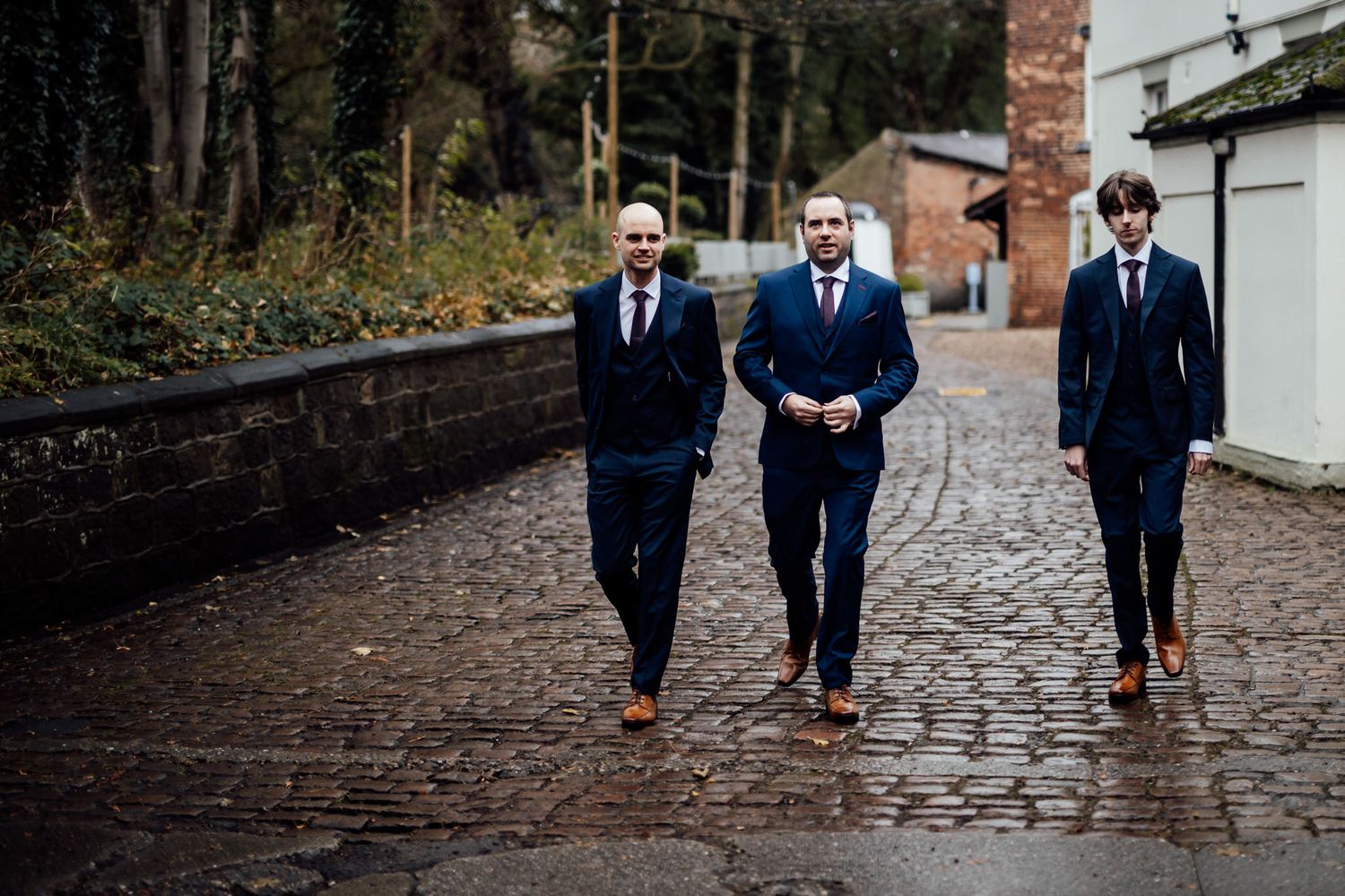 Groomsmen walking together on cobblestone path wearing navy blue suits.