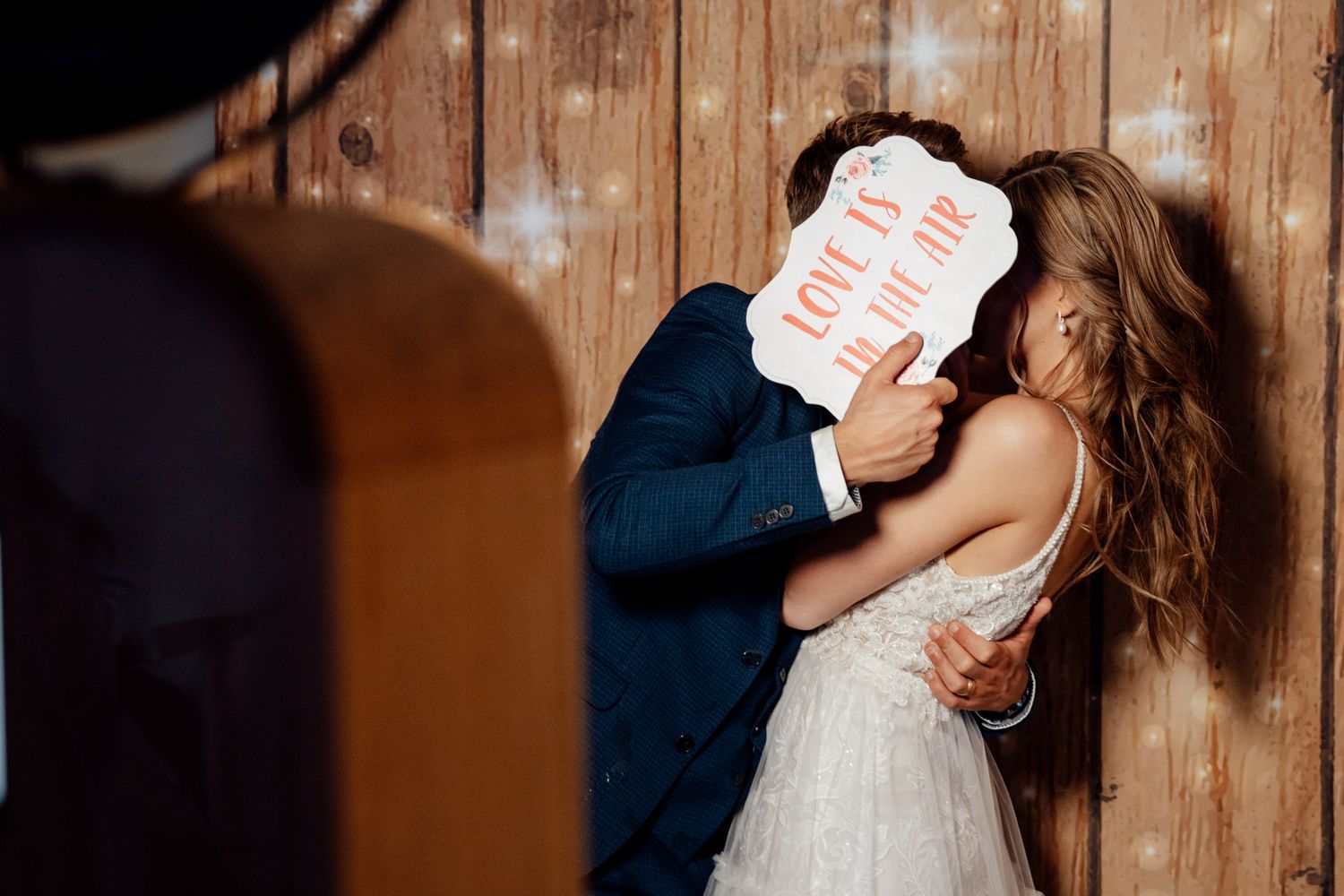 Couple sharing intimate moments during wedding reception against rustic backdrop.