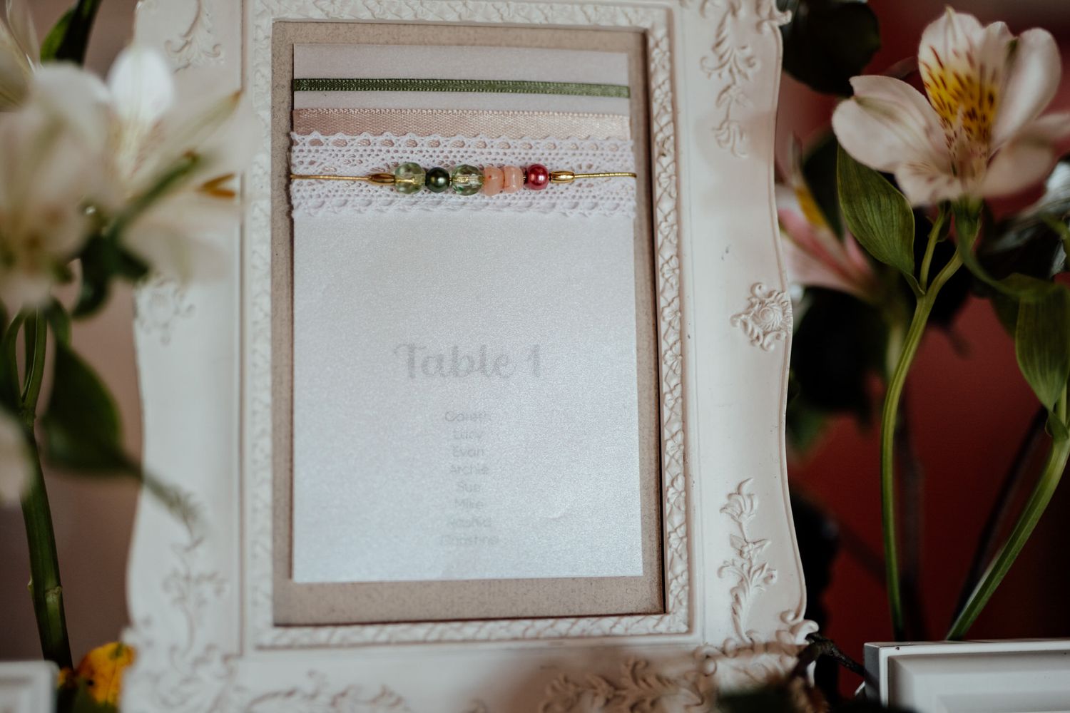 Elegant white framed table seating card with delicate lace detail and floral decorations.