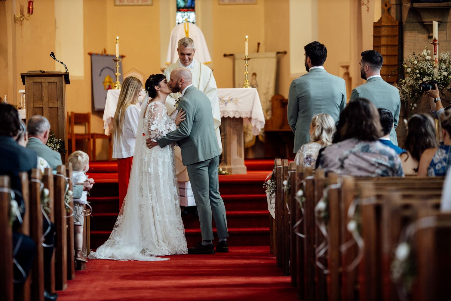 Church interior with yellow walls and wooden pews during wedding ceremony.