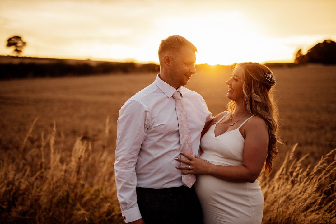 Romantic golden hour portrait of a couple in a field with warm sunset lighting.