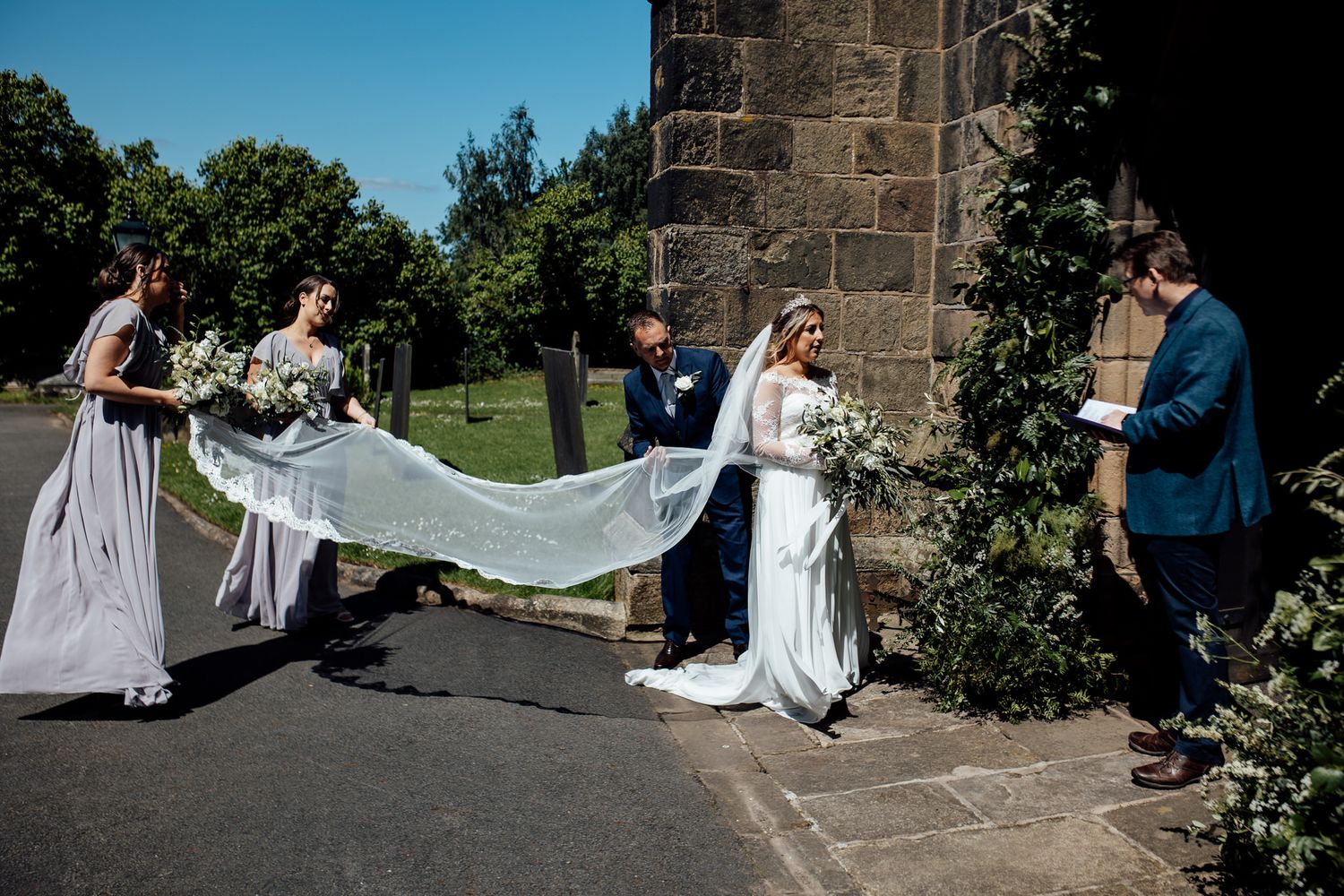 Wedding party gathered outside a historic stone church on a sunny day.