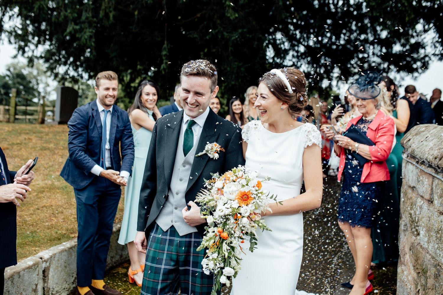 Wedding party and guests celebrate with confetti throwing outside a venue.