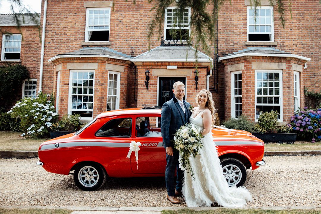 Red vintage car parked outside a historic brick building.