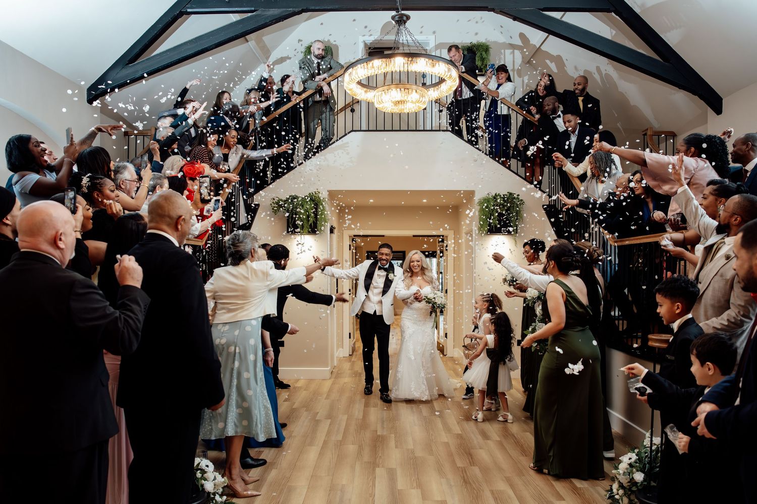 Newlyweds making a grand exit through a confetti shower in an elegant two-story wedding venue.