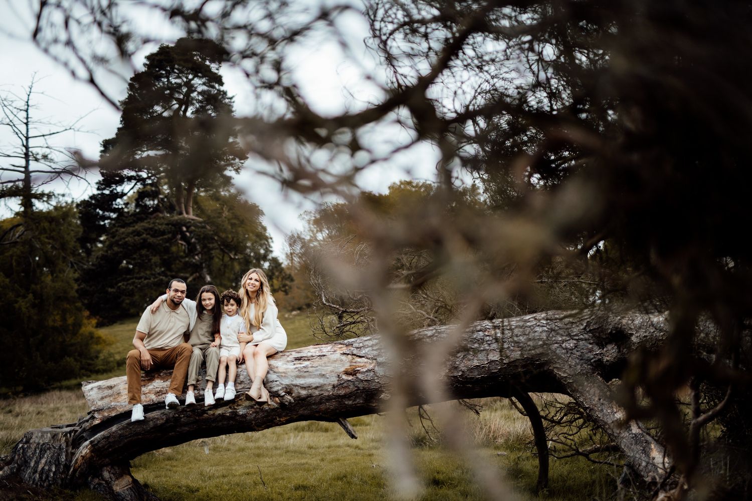 A couple sits together on a fallen tree branch in a scenic outdoor setting.
