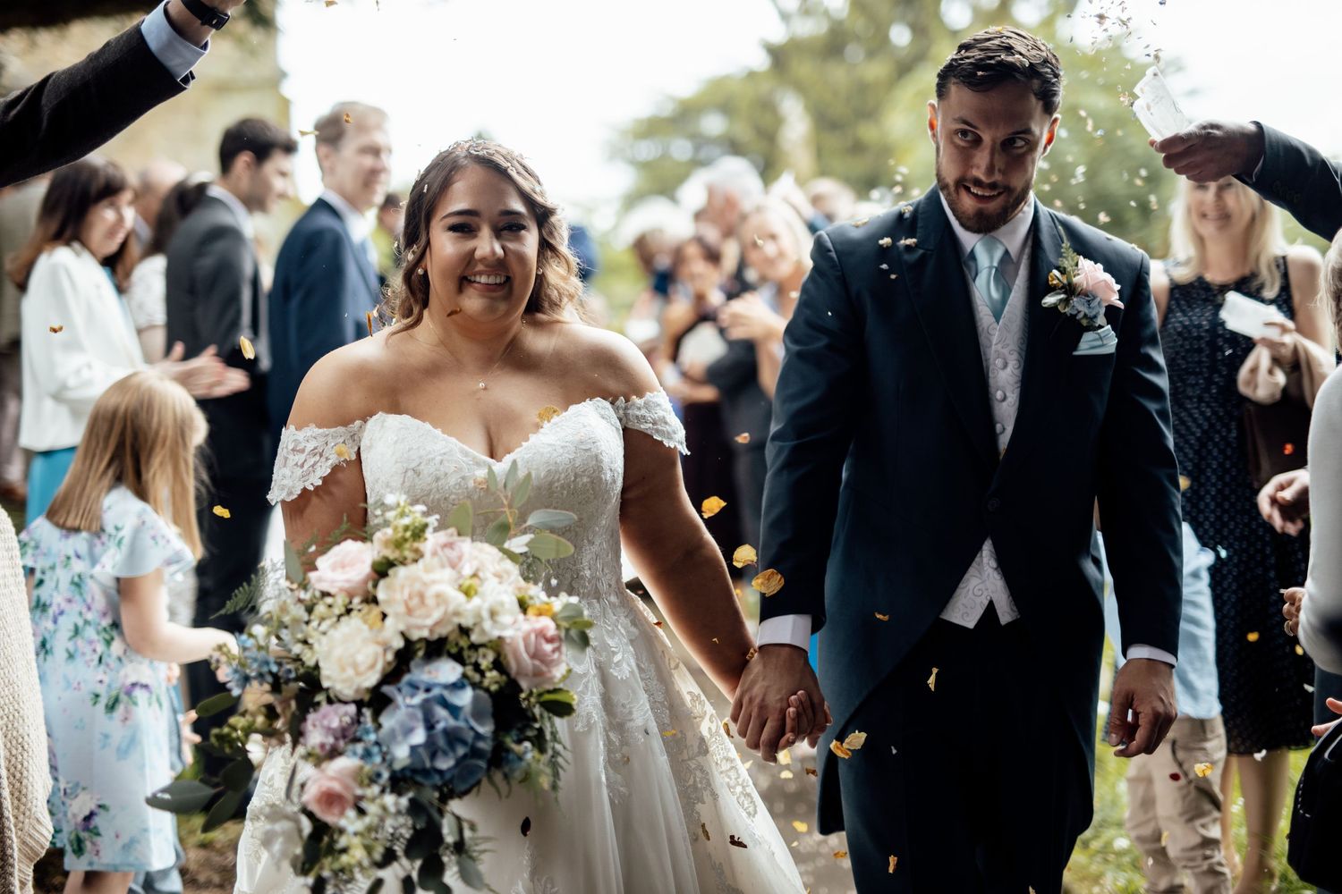 Newlyweds walking down the aisle while guests shower them with confetti.