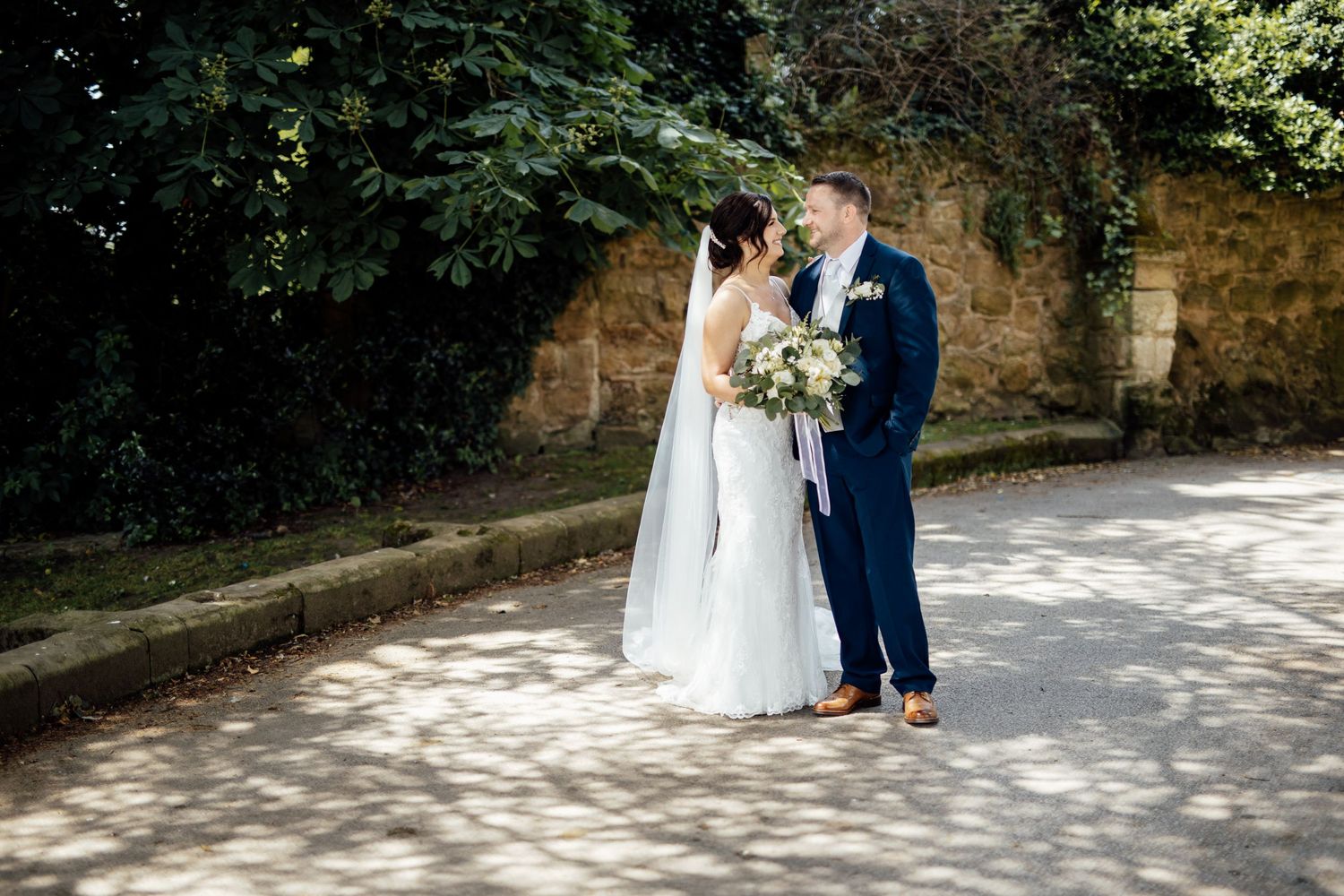 A couple walks along a sunlit stone path during their wedding photoshoot.