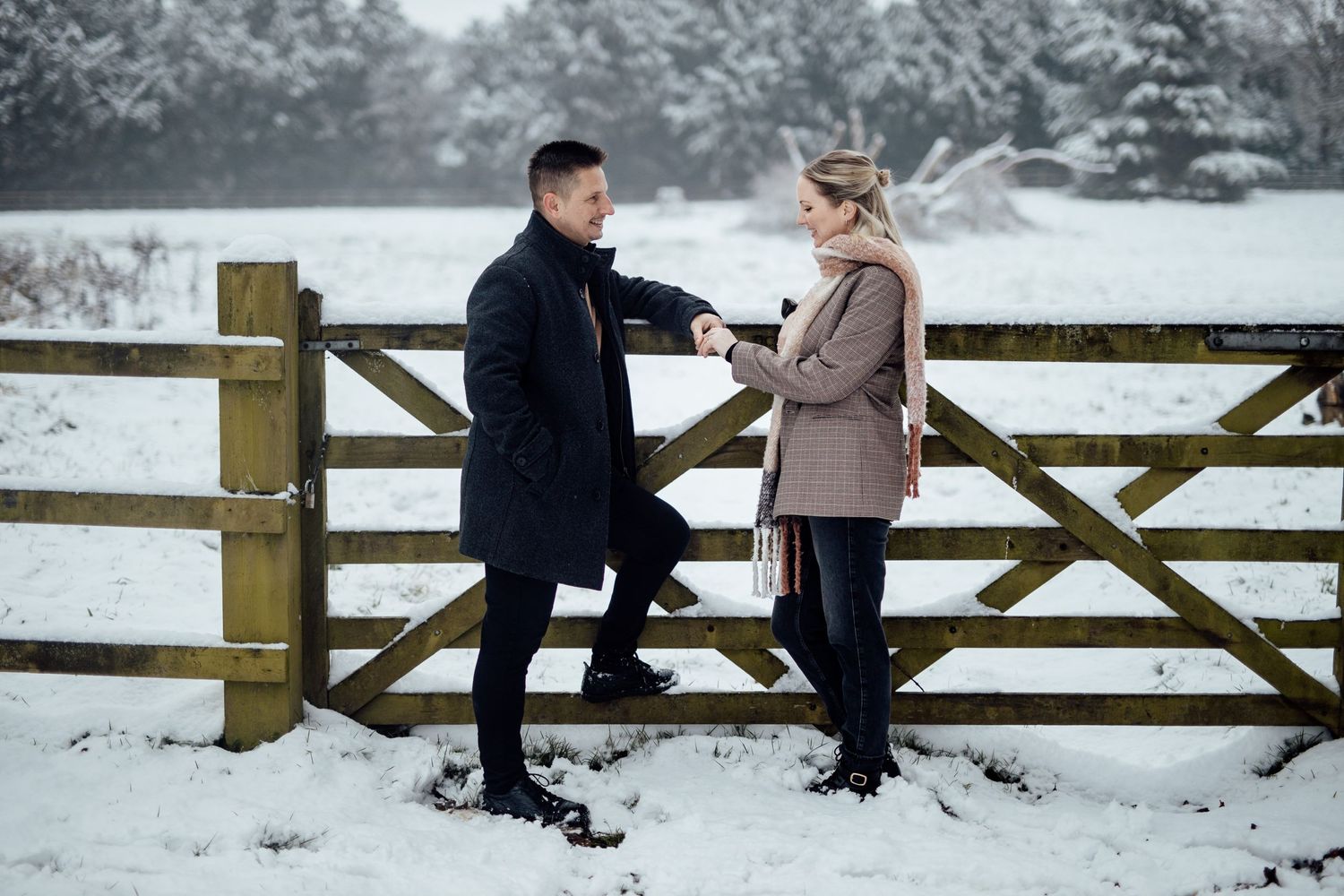 A romantic proposal scene on a wooden gate in a snowy winter landscape.
