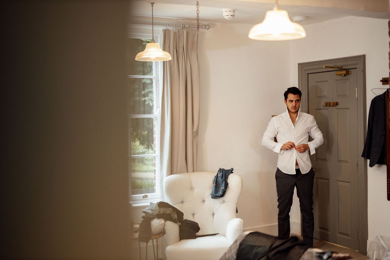 Groomsmen preparing in sunlit room before wedding ceremony.