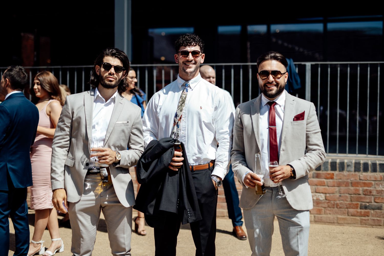 Wedding guests in formal attire enjoying drinks and conversation on an outdoor patio.