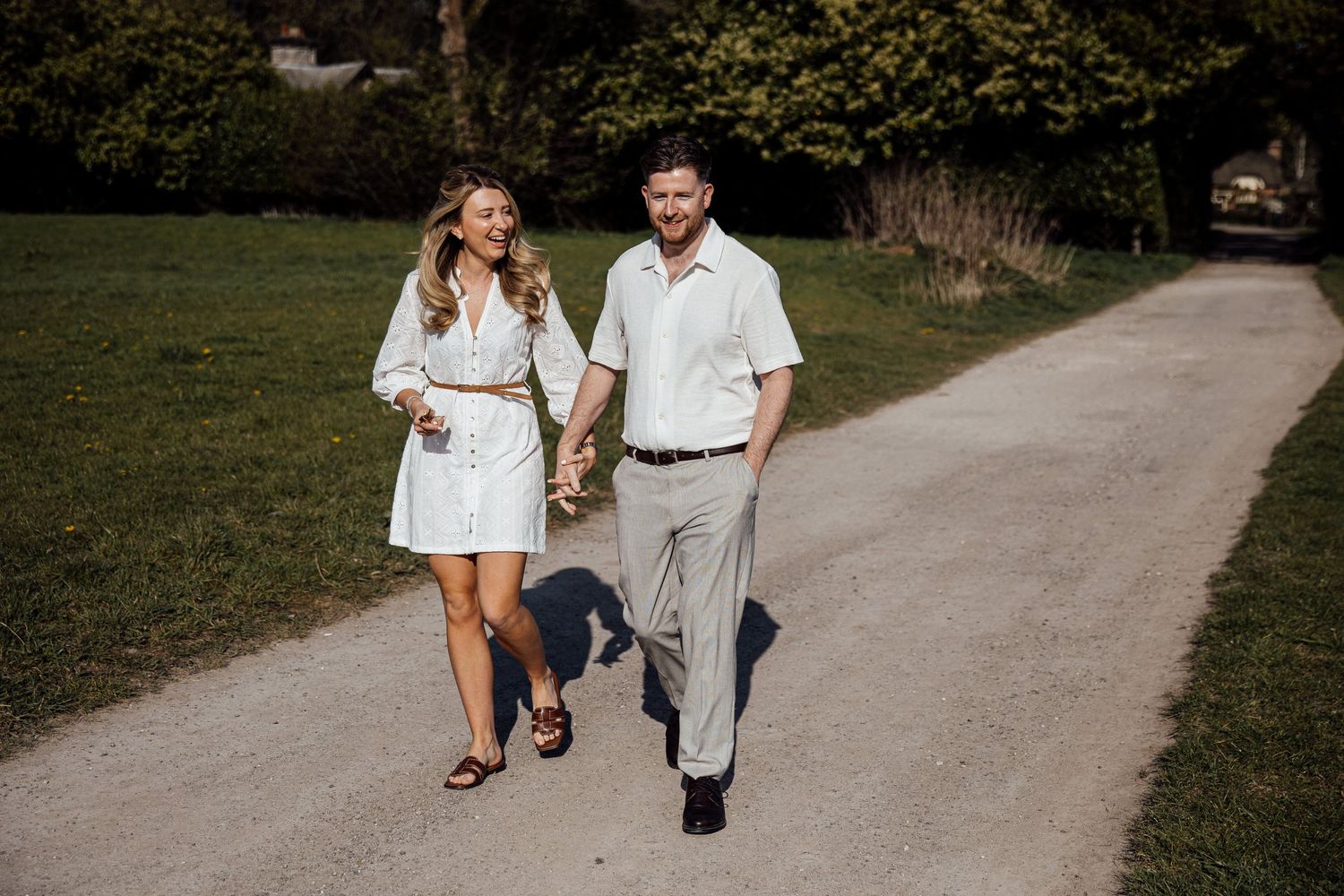 A couple enjoying a casual walk together on a winding gravel path through green fields.