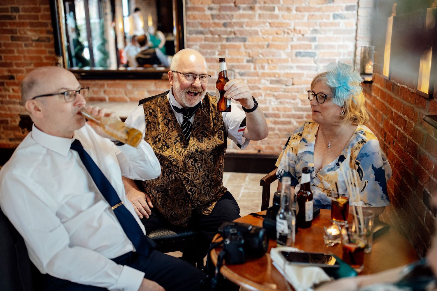 Wedding guests enjoying drinks and conversation at a rustic brick-walled reception venue.