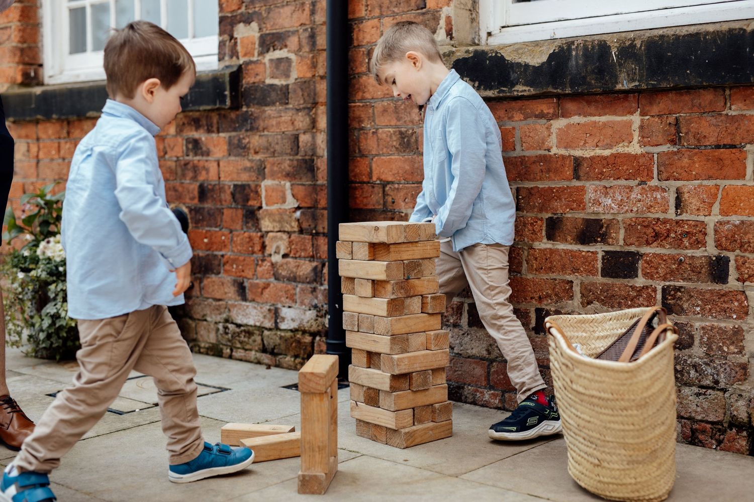 Small child walking past brick wall with wicker basket during wedding.