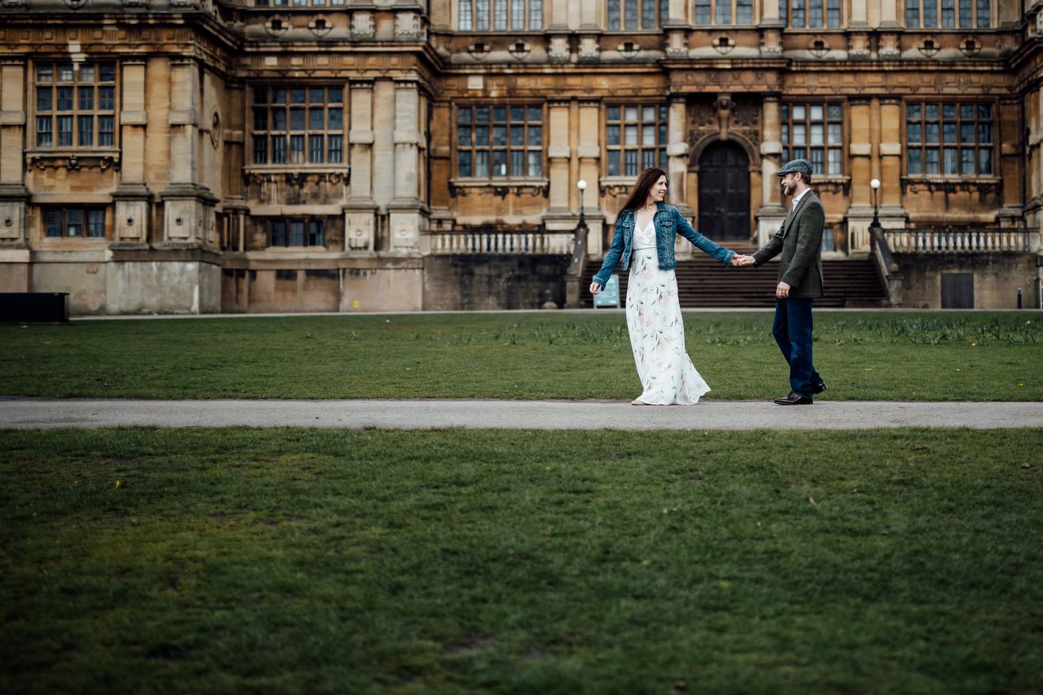 A couple walks hand in hand in front of a grand historic building with ornate architecture.