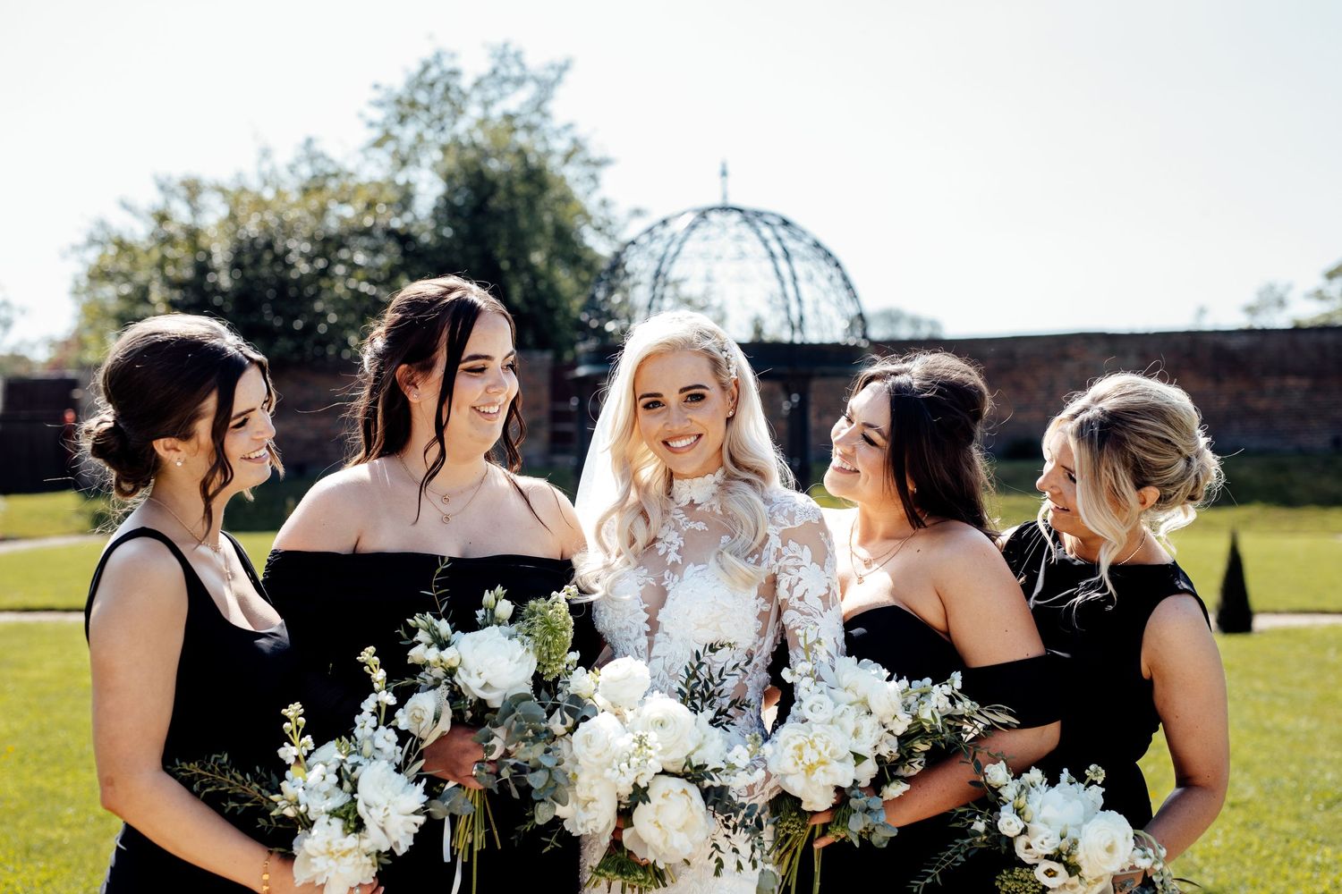 Wedding party holding white floral bouquets poses together outdoors.