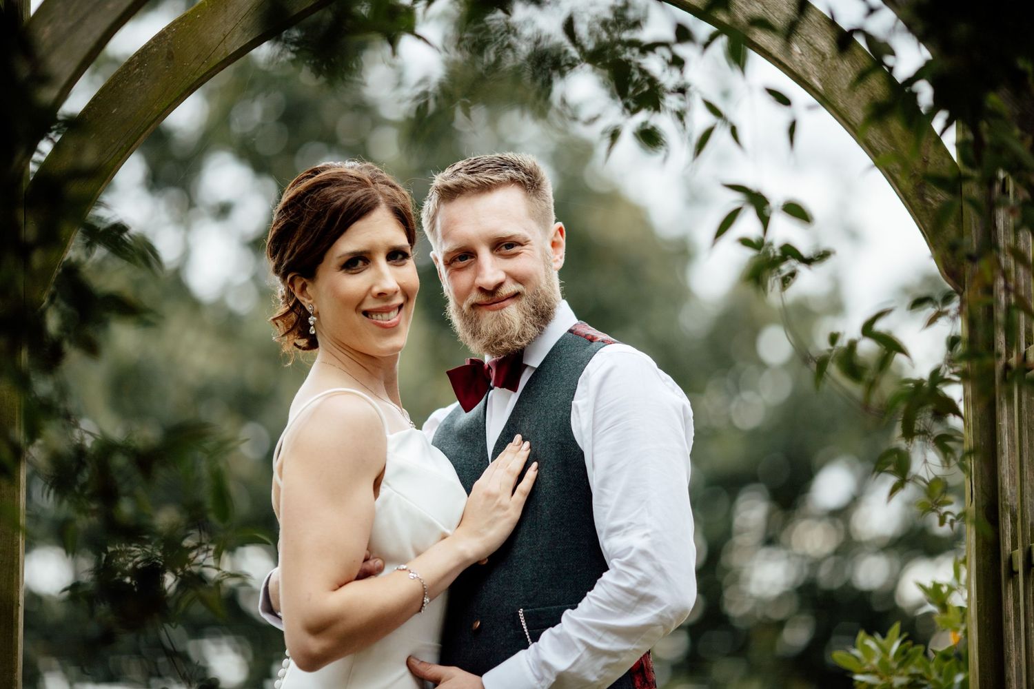 Wedding ceremony under garden arch with greenery and flowers.