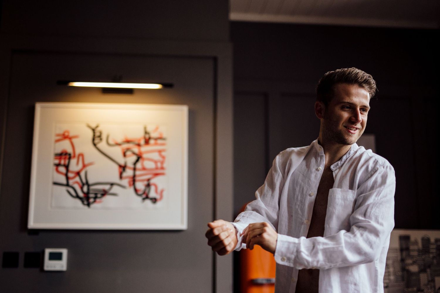 Person in white dress shirt smiling with abstract art on wall in background.