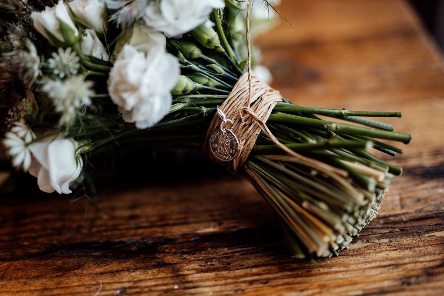 Close-up details of an elegant white floral wedding bouquet with greenery on wooden surface.
