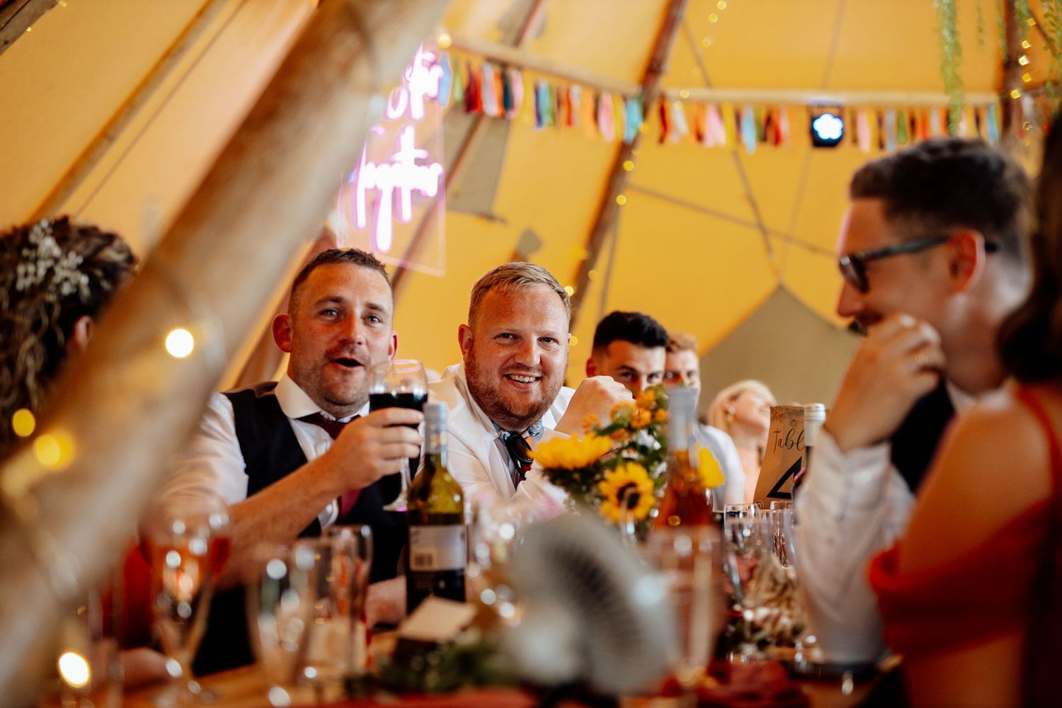 Wedding guests celebrating under warm lighting and festive bunting in a tipi tent.