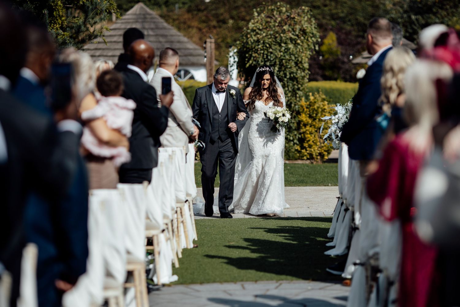 Outdoor garden wedding ceremony with guests seated on white chairs.