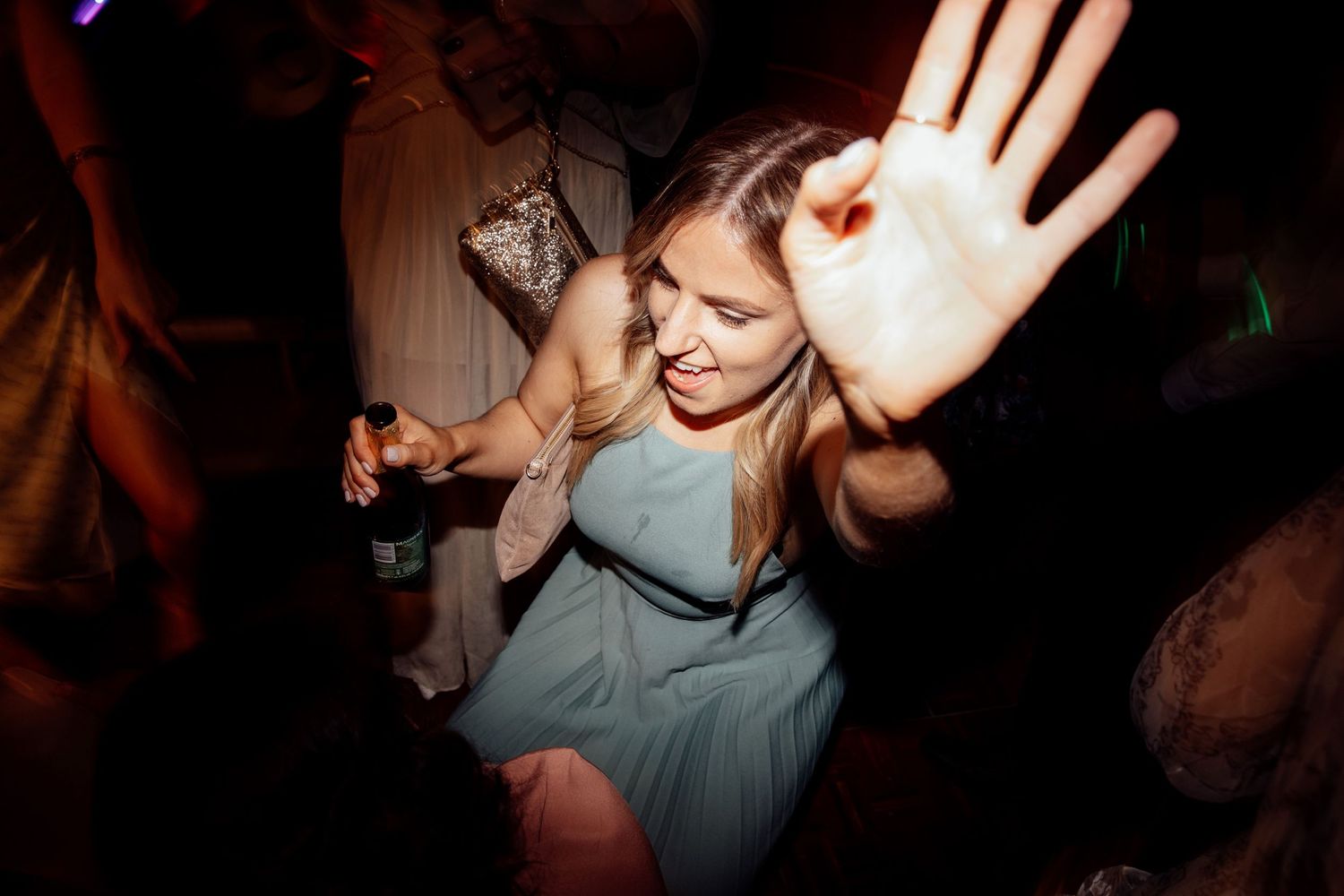Wedding reception party guests dancing and celebrating in dimly lit venue.