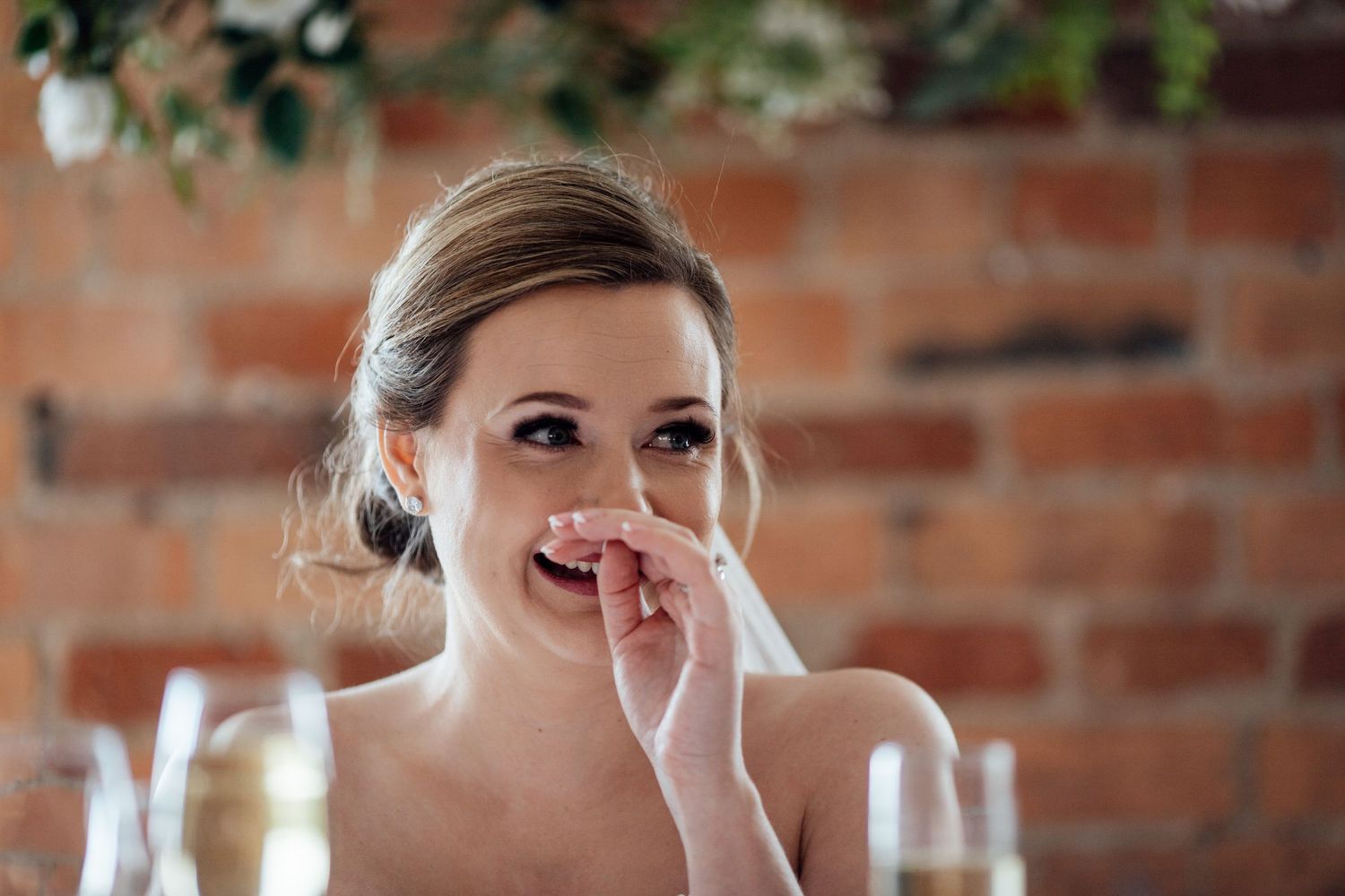 A candid moment of laughter during a wedding celebration against a brick wall backdrop.