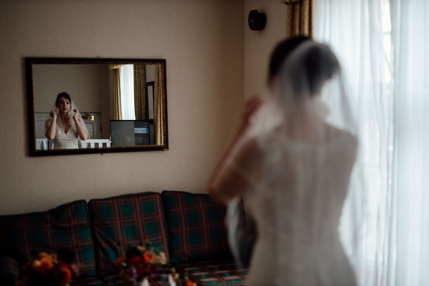 A bride in a white dress looks at her reflection in a mirror during wedding preparations.