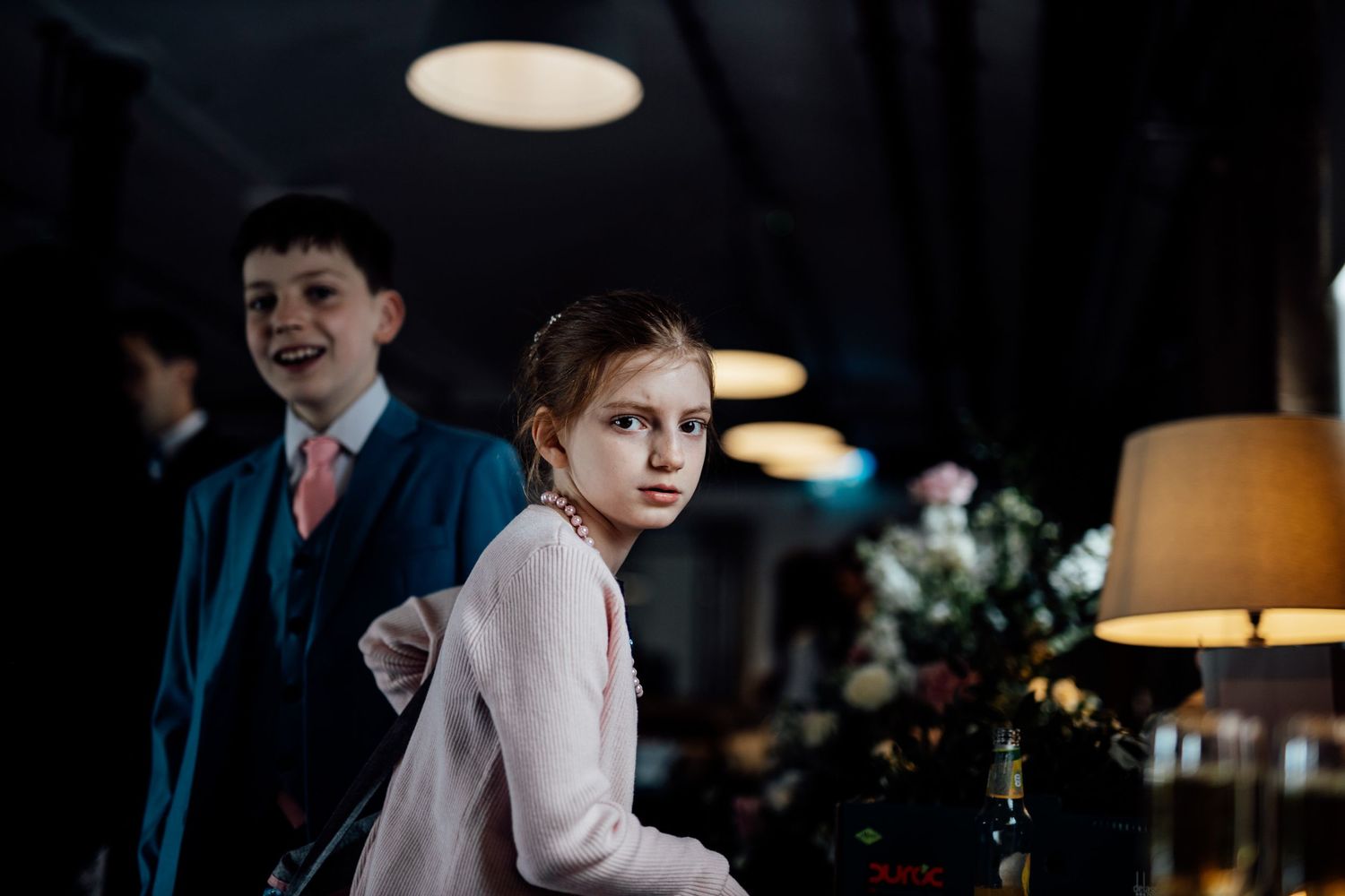 Children at wedding reception venue under moody lighting.