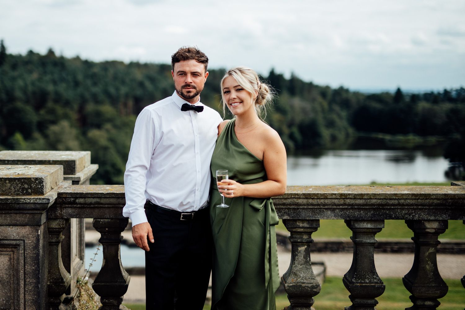 Wedding couple walking along stone balustrade overlooking scenic countryside views.