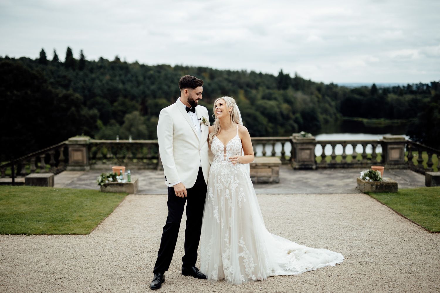 Newlyweds pose on stone terrace overlooking scenic countryside view.