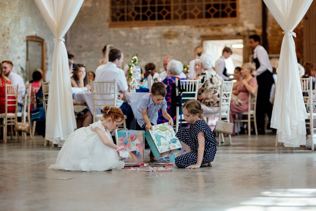 Wedding reception setup in a rustic brick venue with white drapes and table settings.