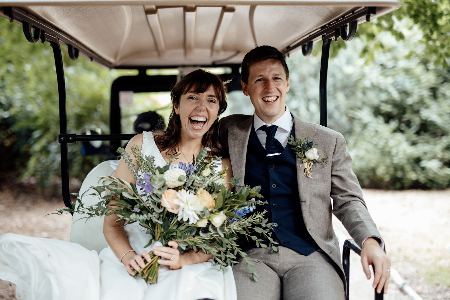 Wedding party riding in a golf cart through a lush green outdoor setting.