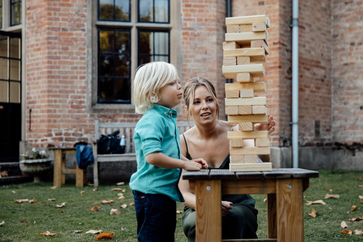 Wedding guests playing giant Jenga outdoors near a brick building.