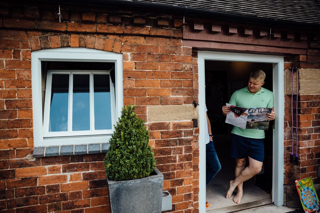 Person standing in doorway of rustic brick building with potted plant by window.