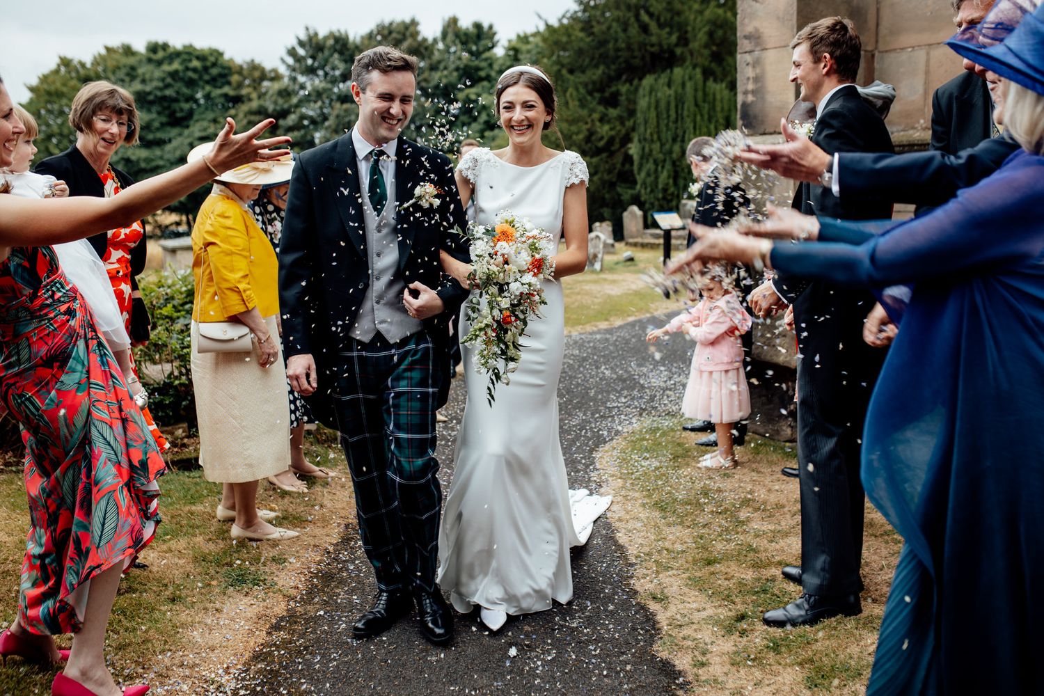 Wedding guests shower the newlyweds with confetti during an outdoor celebration.