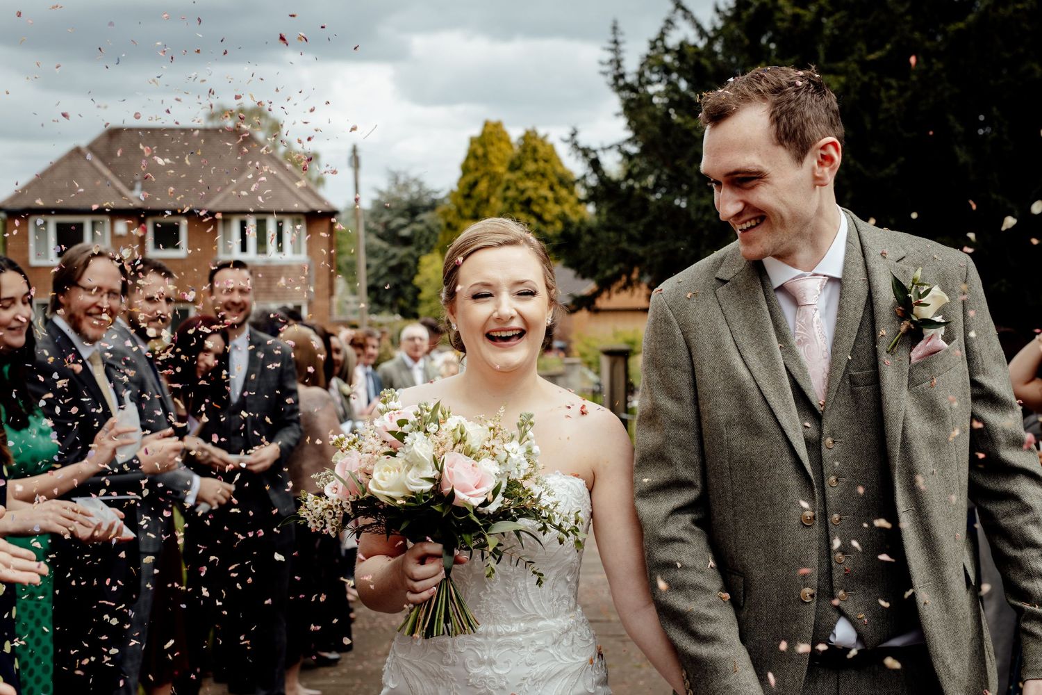 Wedding guests throwing confetti at the happy couple during outdoor celebration.